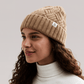 A woman wearing Bouclème Silk Lined Beanie in camel photographed against a soft light grey studio background.