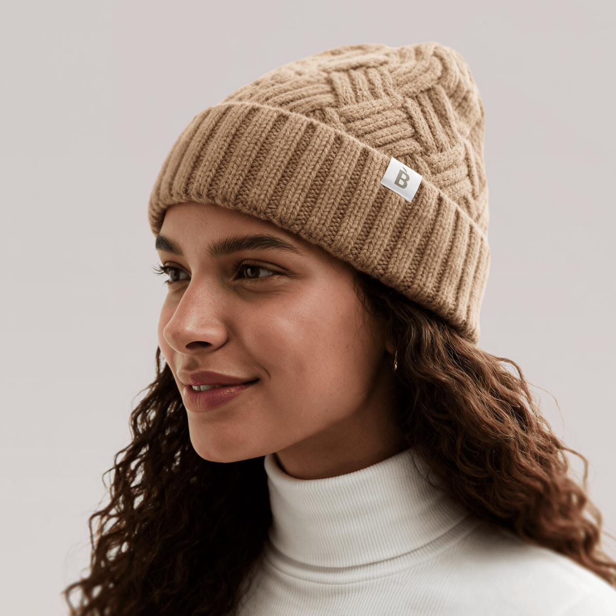 A woman wearing Bouclème Silk Lined Beanie in camel photographed against a soft light grey studio background.