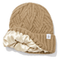 A camel cable-knit beanie hat with a wide cream silk inner lining and a small white square tag on the side.