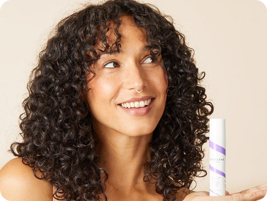 woman with dark-brown curly hair holding a bottle of Bouclème's Protein Booster for curly hair