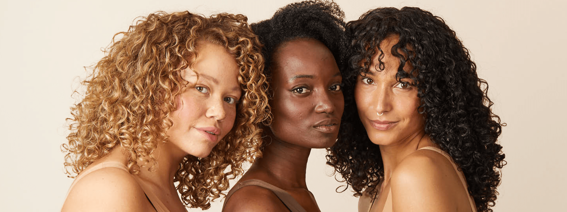 three curly-haired woman standing close together, looking into the camera