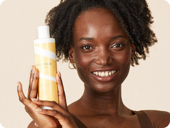 woman with black, coily hair holding a bottle of Bouclème's curl conditioner for curly hair