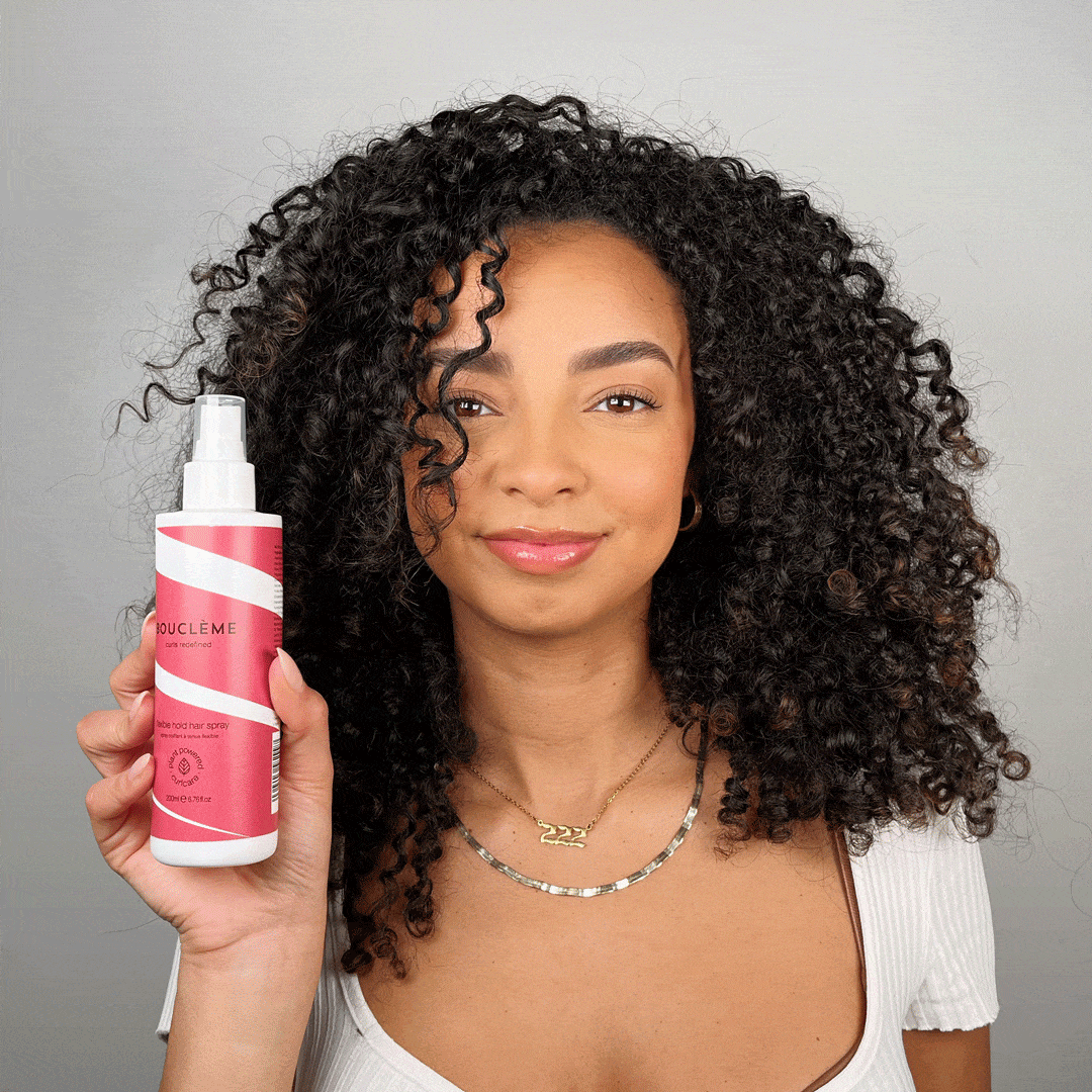 Model applying flexible hold hair spray on dry curly hair to fix the style in place