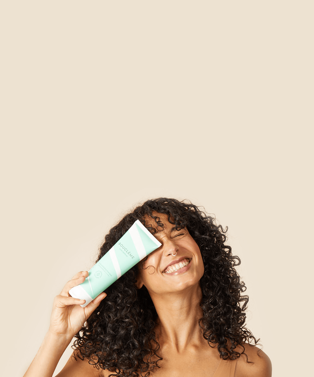 woman with curly hair grinning whilst holding up a bottle of Bouclème's Scalp Exfoliating Shampoo